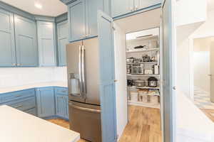 Kitchen featuring light countertops, stainless steel fridge with ice dispenser, blue cabinets, decorative backsplash, and light wood finished floors