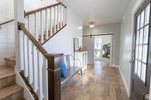 Foyer entrance featuring hardwood / wood-style floors, a barn door, stairs, and wooden walls