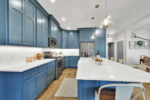 Kitchen featuring stainless steel appliances, a kitchen bar, blue cabinets, light wood-style floors, and recessed lighting