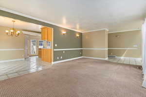 Unfurnished room with light carpet, a chandelier, ornamental molding, and light tile patterned floors