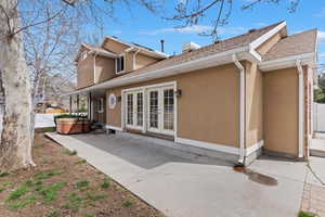 Rear view of property featuring stucco siding, a hot tub, french doors, a patio area, and a chimney
