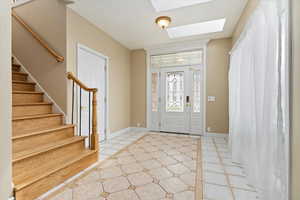 Foyer entrance with light tile patterned floors, a skylight, stairway, and baseboards