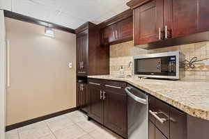 Kitchen featuring light tile patterned flooring, baseboards, appliances with stainless steel finishes, a sink, and backsplash