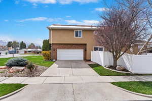 View of front of house with concrete driveway, stucco siding, fence, a front lawn, and a garage