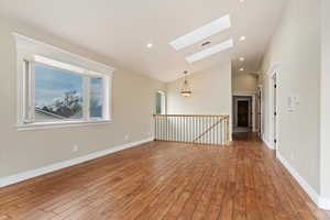 Empty room featuring baseboards, wood finished floors, lofted ceiling with skylight, and recessed lighting