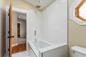 Bathroom featuring vaulted ceiling, toilet, marble finish floor, baseboards, and a combined bath / shower with rainfall shower