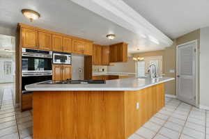 Kitchen featuring light countertops, stainless steel appliances, a spacious island, a sink, and brown cabinetry