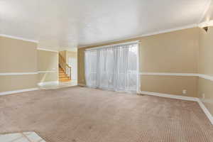 Unfurnished living room featuring ornamental molding, carpet, baseboards, and stairway