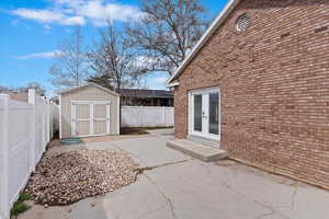View of patio featuring french doors, a fenced backyard, an outdoor structure, and a storage shed