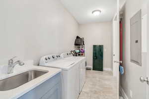 Clothes washing area featuring separate washer and dryer, light tile patterned flooring, a sink, laundry area, and electric panel