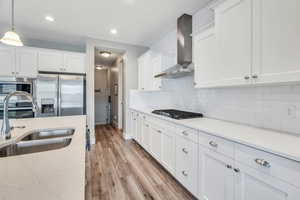 Kitchen featuring white cabinets, stainless steel appliances, tasteful backsplash, a sink, and wall chimney range hood
