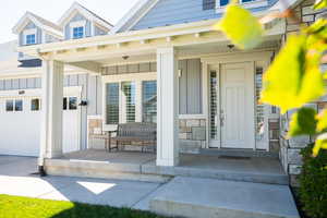 View of exterior entry with stone siding, a garage, board and batten siding, and a porch