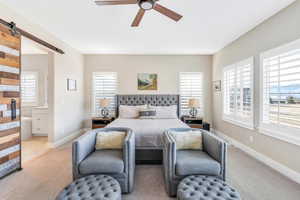 Bedroom with ensuite bathroom, baseboards, a ceiling fan, a barn door, and light colored carpet