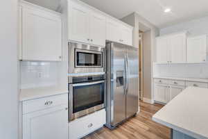 Kitchen with white cabinetry, light wood-style flooring, appliances with stainless steel finishes, and decorative backsplash