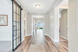 Hall with baseboards, a barn door, and light wood finished floors