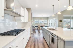 Kitchen featuring a sink, tasteful backsplash, wood finished floors, appliances with stainless steel finishes, and wall chimney range hood