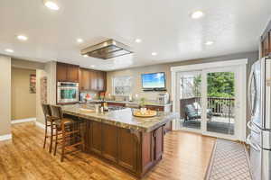 Kitchen featuring stainless steel appliances, a kitchen island with sink, light wood finished floors, and a kitchen breakfast bar