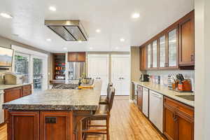 Kitchen with glass insert cabinets, light wood-type flooring, a breakfast bar area, and stainless steel appliances