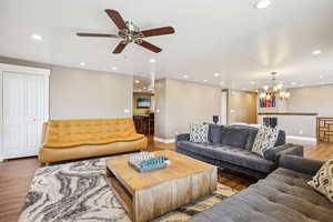 Living room with recessed lighting, ceiling fan with notable chandelier, baseboards, and wood finished floors