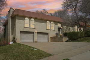 View of front facade with brick siding, a chimney, an attached garage, and concrete driveway