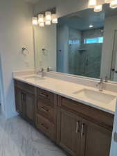 Primary Suite bath with double vanity, a marble finish shower, and marble look tile flooring