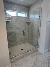Primary Suite Bath: featuring a marble finish shower and marble finish flooring