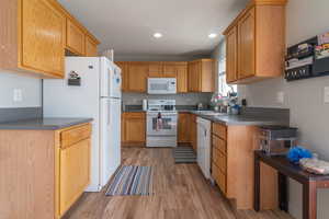 Kitchen featuring white appliances, recessed lighting, wood finished floors, and a sink
