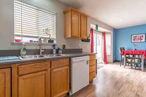 Kitchen with a sink, white dishwasher, dark countertops, and light wood finished floors