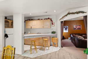 Kitchen featuring light wood finished floors, a kitchen breakfast bar, light brown cabinets, tile countertops, and recessed lighting