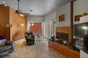 Living room with a ceiling fan, a fireplace, wood finished floors, a textured ceiling, and baseboards
