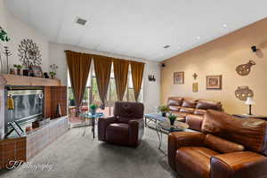 Living area with visible vents, a tiled fireplace, carpet, and vaulted ceiling