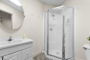 Full bathroom featuring a shower stall, baseboards, wood finished floors, toilet, and vanity