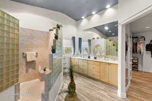 Bathroom featuring double vanity, wood finished floors, a sink, vaulted ceiling, and a walk in shower