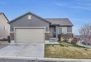 View of front of home with concrete driveway, stucco siding, stone siding, a front lawn, and a garage