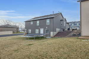 Back of house with central air condition unit, a trampoline, stucco siding, a mountain view, and a yard