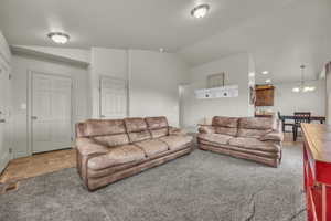 Living area featuring visible vents, vaulted ceiling, an inviting chandelier, and light carpet