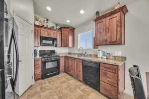 Kitchen featuring light stone countertops, recessed lighting, a sink, black appliances, and brown cabinetry