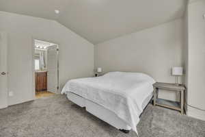 Bedroom featuring light carpet, vaulted ceiling, and connected bathroom