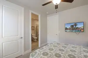 Bedroom with ensuite bathroom, carpet flooring, baseboards, and a ceiling fan