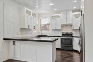 Kitchen featuring white cabinetry, a peninsula, under cabinet range hood, stainless steel appliances, and dark wood-type flooring