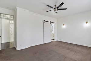 Spare room featuring a ceiling fan, a barn door, crown molding, and dark colored carpet