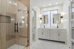 Full bathroom featuring a shower stall, double vanity, toilet, and a sink