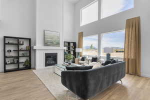 Living room featuring baseboards, wood finished floors, a towering ceiling, and a glass covered fireplace