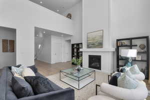 Living area with baseboards, a towering ceiling, wood finished floors, and a glass covered fireplace