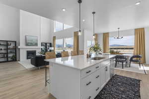 Kitchen featuring white cabinets, light wood finished floors, a sink, a glass covered fireplace, and an inviting chandelier