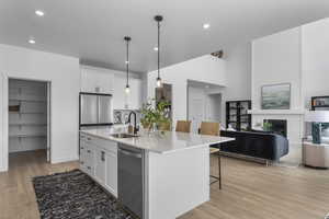 Kitchen with a kitchen bar, stainless steel appliances, a sink, an island with sink, and white cabinets