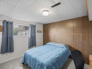 Bedroom with baseboards, visible vents, wooden walls, and carpet