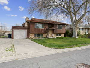 Bi-level home with concrete driveway, a chimney, brick siding, a front lawn, and a garage