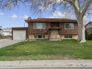 Raised ranch featuring a chimney, brick siding, a front yard, and an attached garage
