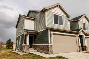 Craftsman inspired home featuring board and batten siding, stone siding, a garage, and concrete driveway